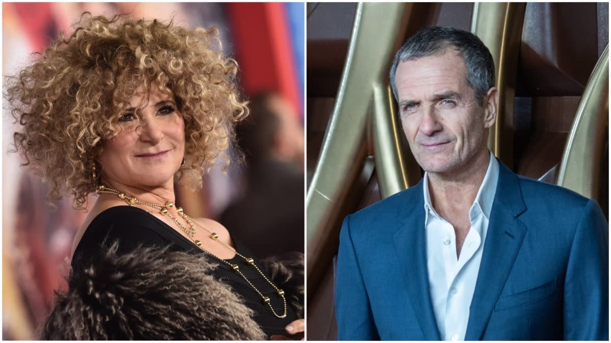 Amy Pascal, a woman with curly hair and wearing a black outfit, smiles on the left, while David Heyman, a man in a blue suit with short hair, poses on the right. This image highlights the producers of the next James Bond film.