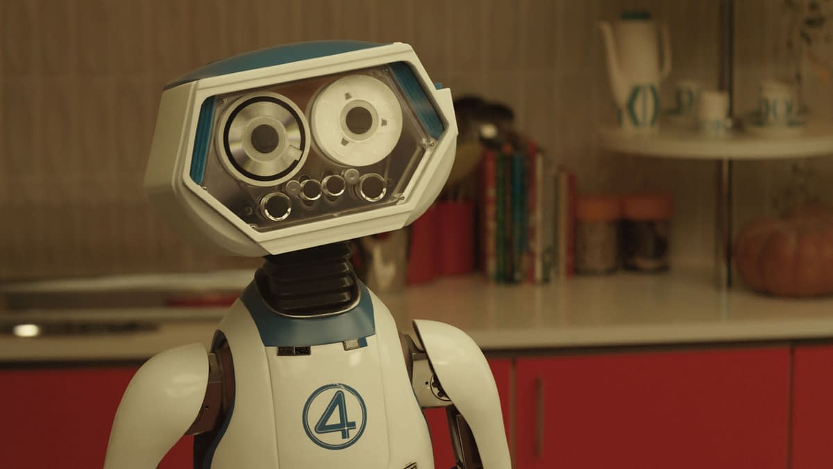 A friendly robot character named H.E.R.B.I.E stands in a modern kitchen setting, featuring a bright red cabinetry and various kitchen items in the background. The design includes a distinctive blue and white color scheme with the number '4' displayed, representing its connection to Marvel's 'The Fantastic Four: First Steps'.