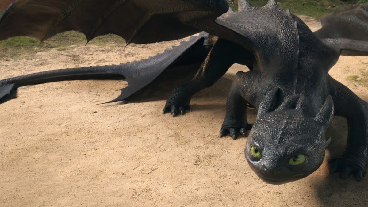 A stylized dragon with glossy black scales and large green eyes is crouched on a sandy surface, its wings partially extended. The scene appears to be set in a natural outdoor environment.