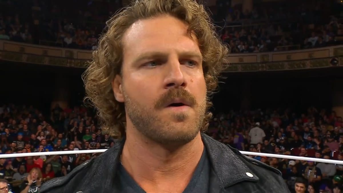Hangman Adam Page, a professional wrestler, appears on stage at AEW Dynamite, displaying a serious expression with a crowd in the background.