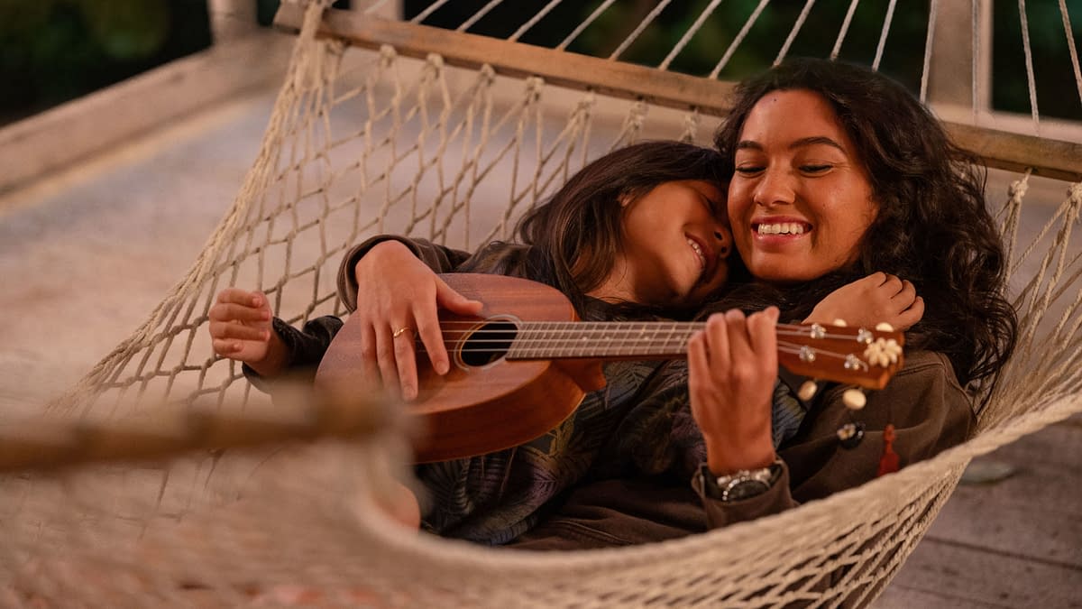 Two young women relax together in a hammock, with one playing a ukulele. The scene captures a warm and intimate moment, highlighting the bond between Lilo and her older sister Nani from Disney's live-action adaptation of 'Lilo & Stitch.'