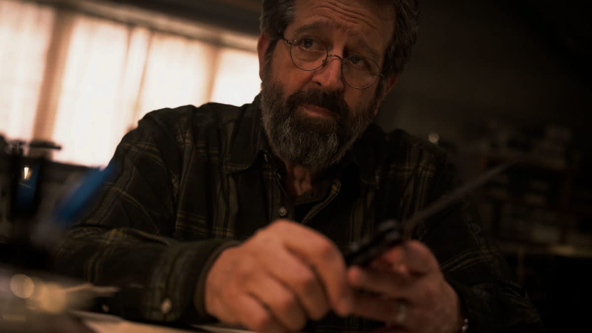 A scene from 'Mission: Impossible - The Final Reckoning' featuring Rolf Saxon as William Donloe, who appears contemplative while holding a pair of scissors in a dimly lit room.