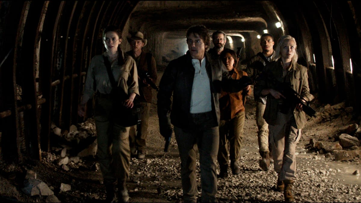 A scene from 'Mission: Impossible - The Final Reckoning' featuring a group of seven characters walking through a dimly lit underground passage, dressed in tactical gear and appearing focused and alert.