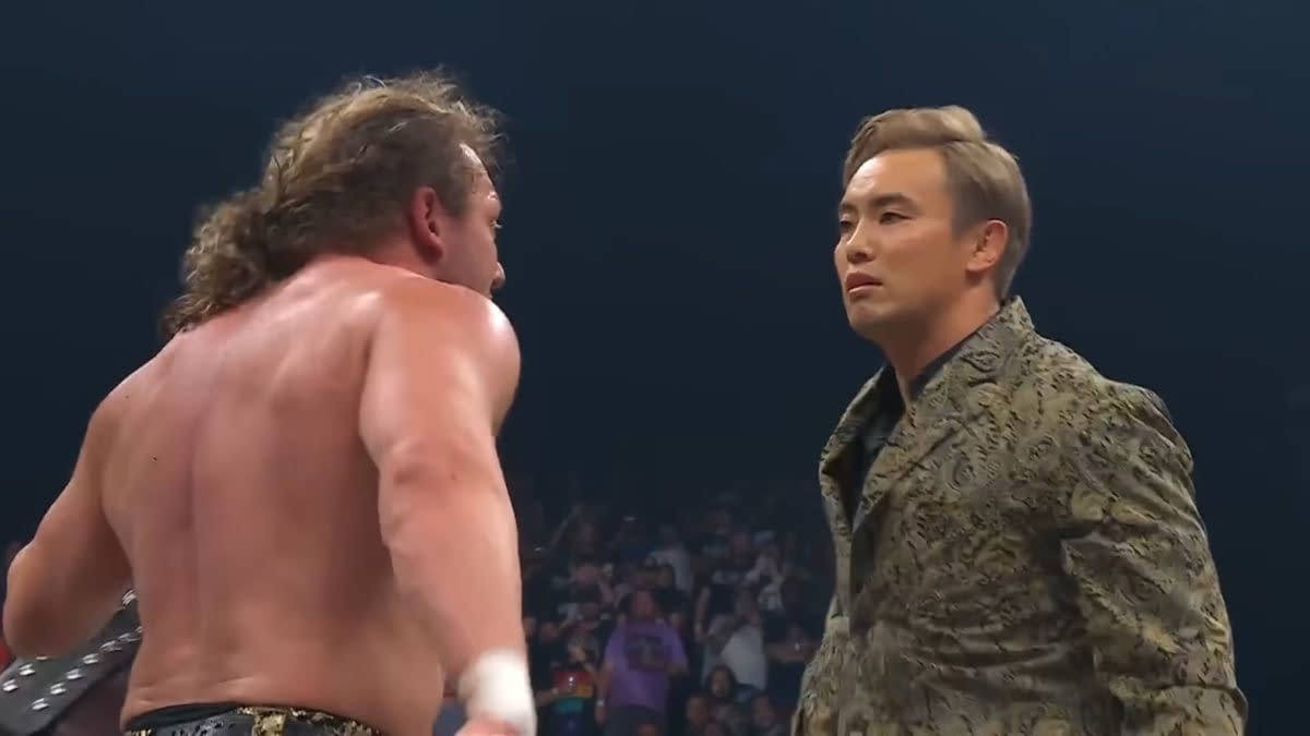 Kenny Omega and Kazuchika Okada face each other intensely during AEW Fyter Fest, capturing a moment of confrontation between two wrestling stars. Omega, with his long hair and muscular physique, faces Okada, who is dressed in an ornate jacket, emphasizing the tension of their rivalry.