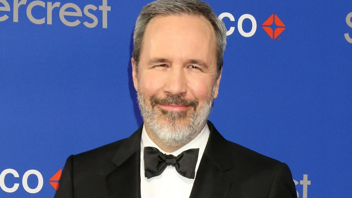 A man with a beard, wearing a tuxedo with a bow tie, smiles in front of a blue backdrop featuring the text 'silvercrest' and a logo. The setting appears elegant, suggesting a formal event.
