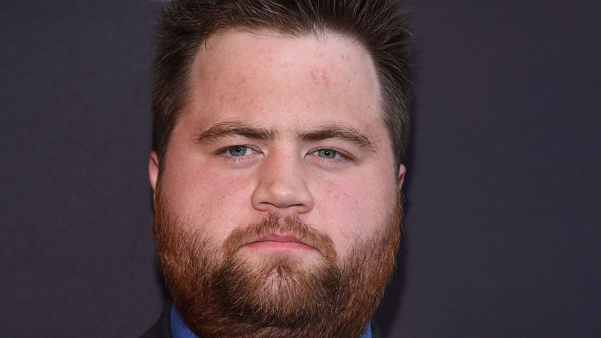Actor Paul Walter Hauser with a beard and close-cropped hair, poses against a dark background at the "Kingdom" Season 2.5 Premiere in Los Angeles.