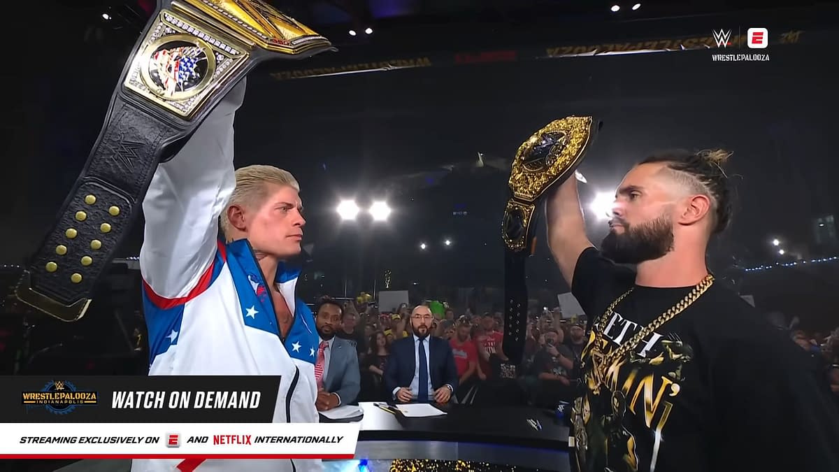 Cody Rhodes and Seth Rollins hold up their championship belts triumphantly after WWE WrestlePalooza, with a cheering crowd in the background. The scene captures the excitement of the event with lights shining above.