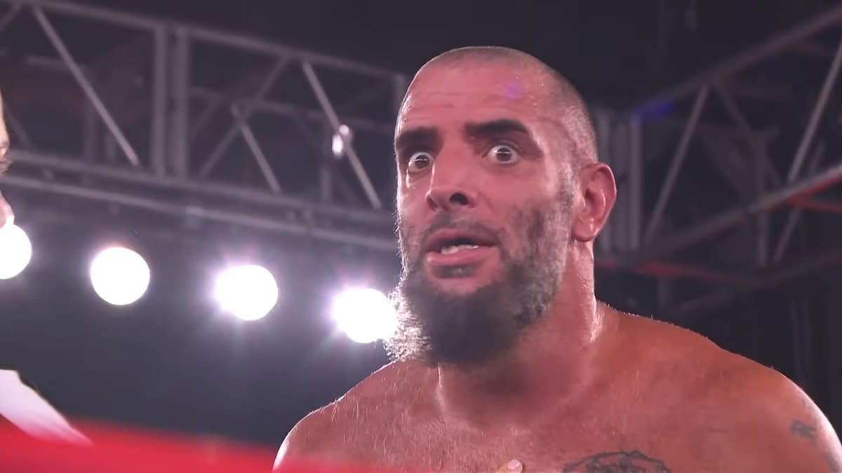 A close-up of Mark Briscoe with an astonished expression while engaged in a scene on AEW Collision, surrounded by bright stage lights.
