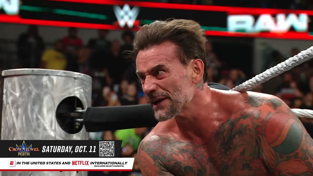 A visibly upset wrestler, with tattoos covering his torso, is yelling while gripping the ropes in a wrestling ring on WWE Raw. The audience can be seen in the background, along with promotional graphics for an upcoming event.