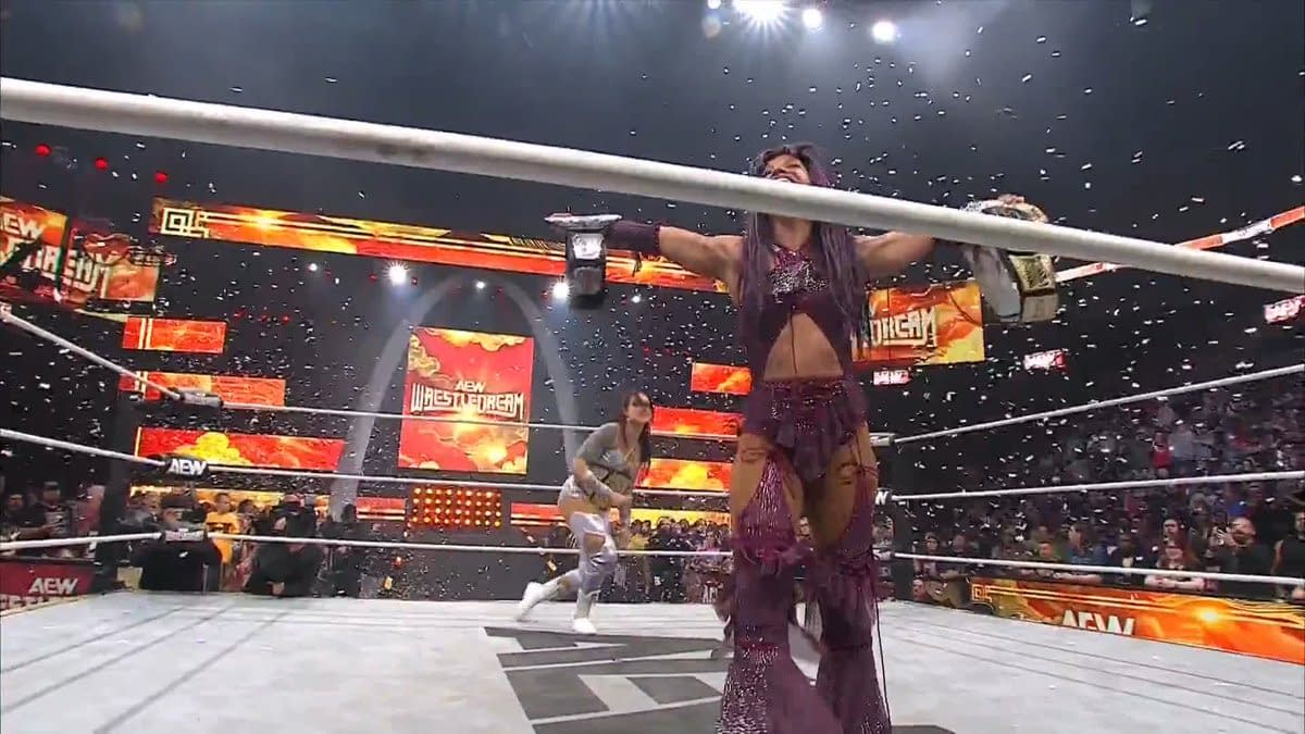 Kris Statlander appears in a wrestling ring at AEW WrestleDream, poised to confront Mercedes Moné, who holds the championship belt. Confetti is falling in the background as fans cheer.