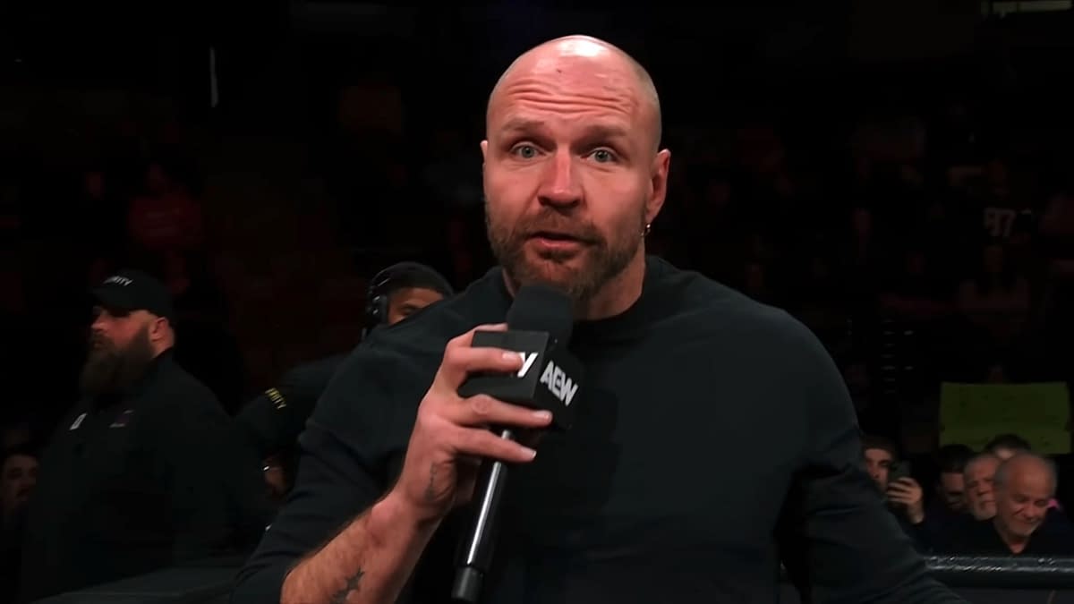 Jon Moxley delivering a promo on AEW Collision, holding a microphone while speaking to the audience. The background includes fans watching attentively.
