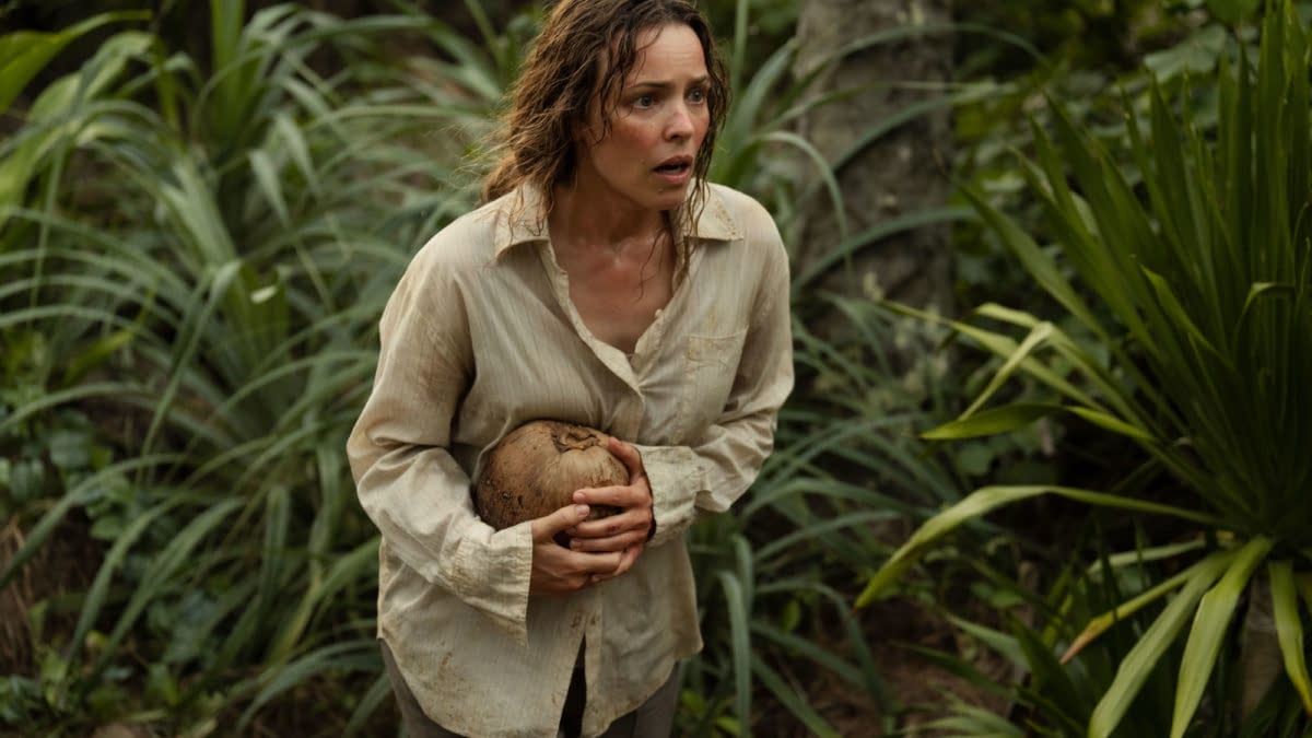Rachel McAdams portrays Linda Liddle in a tense moment from 20th Century Studios' film 'SEND HELP,' showing her with a distressed expression while holding a coconut, surrounded by dense greenery.