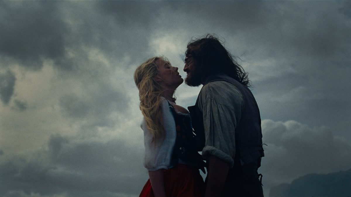 A dramatic scene from 'Wuthering Heights' featuring a man and a woman leaning towards each other against a moody, cloudy sky. The woman has long blonde hair, while the man has a rugged look with a beard.