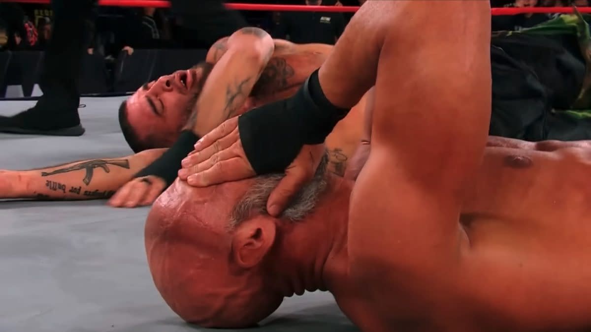 Tommaso Ciampa lies on the mat with his head down, while Mark Briscoe is sprawled on the floor with a pained expression. Both wrestlers appear exhausted after a physically demanding TNT title match.