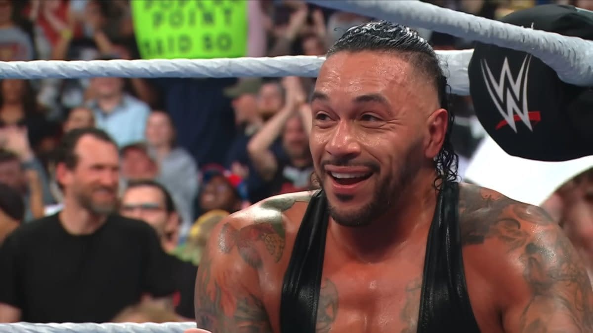 Damian Priest smiles broadly, expressing delight after winning his match during WWE SmackDown, with a cheering crowd in the background.