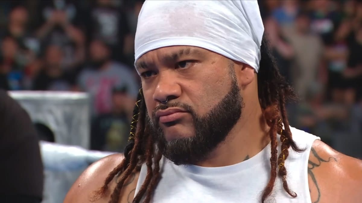 Jacob Fatu stands in the ring on WWE SmackDown, wearing a white head covering and sleeveless top with a stern expression.