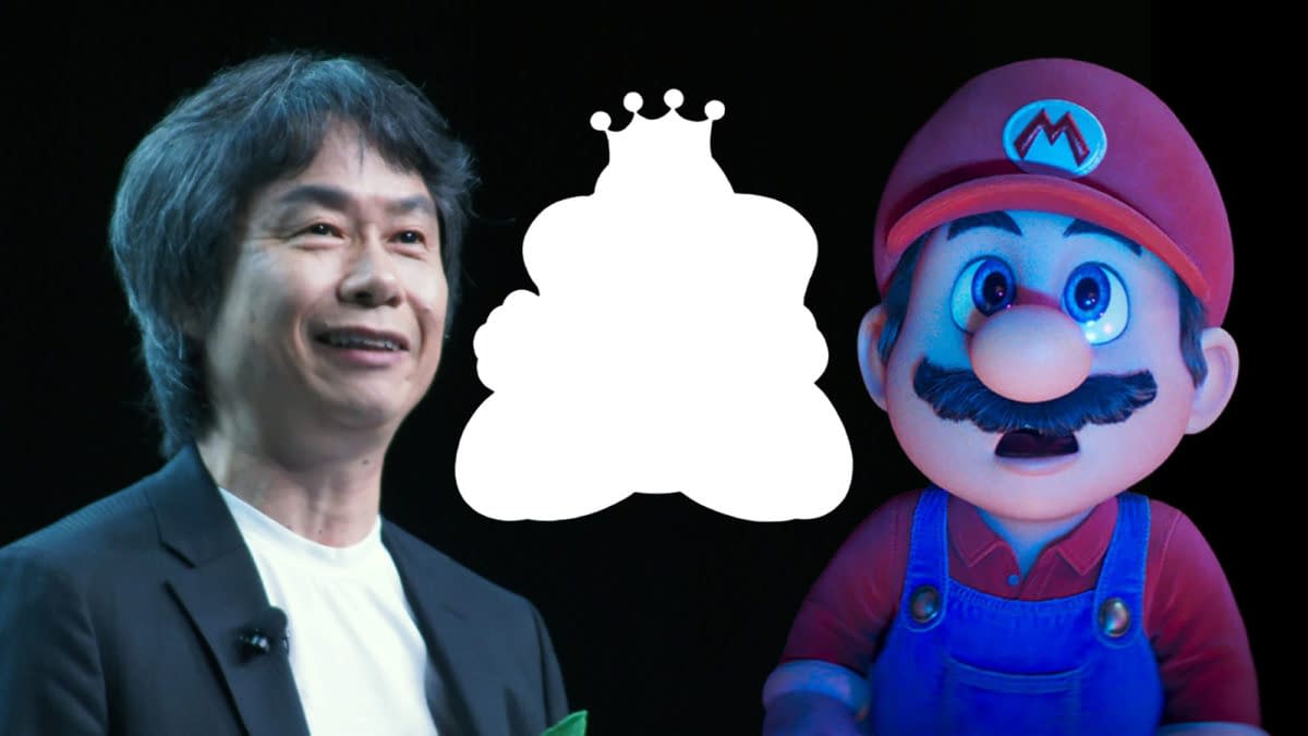 Shigeru Miyamoto smiles while standing next to a cartoon character resembling Mario, the iconic figure from Nintendo, with a blurred background. The image captures a moment from an E3 gaming conference.