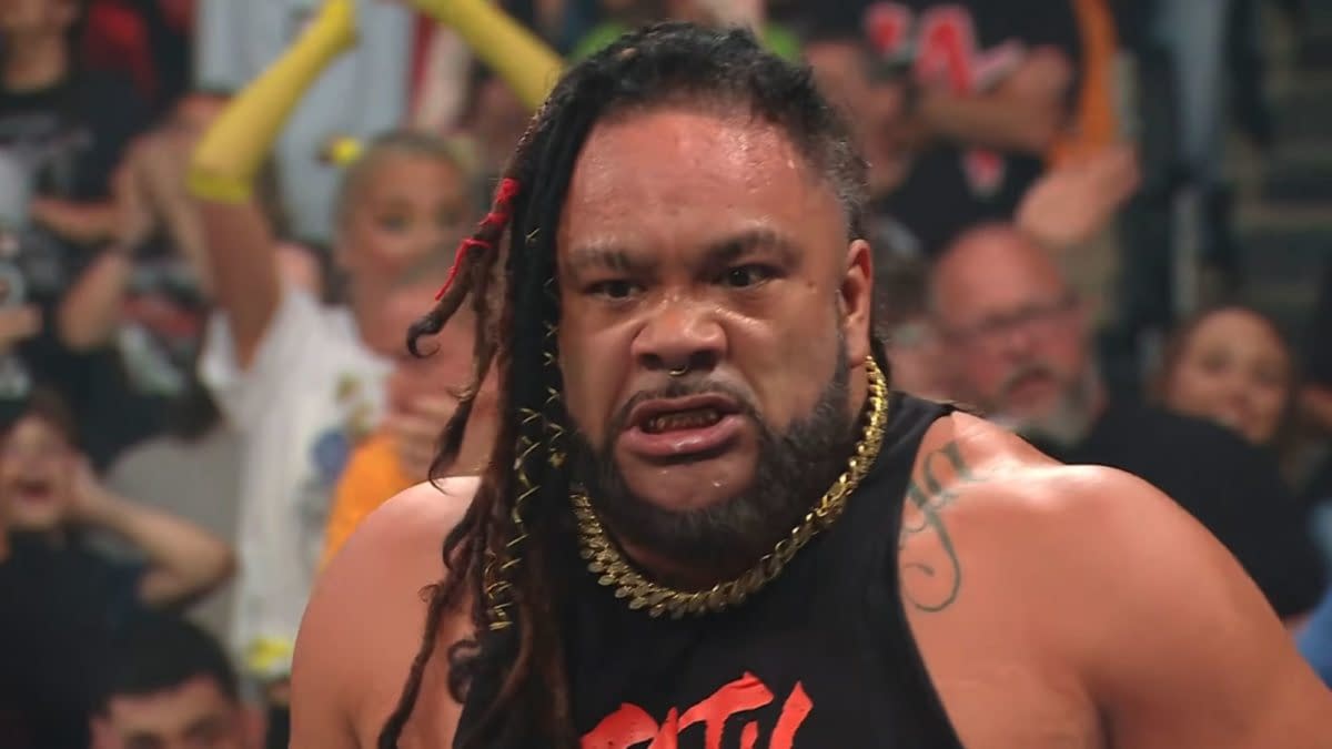 Jacob Fatu glares intensely in the WWE Raw ring, looking enraged after a chaotic moment. He wears a black sleeveless top and gold chain, with the crowd blurred behind him.