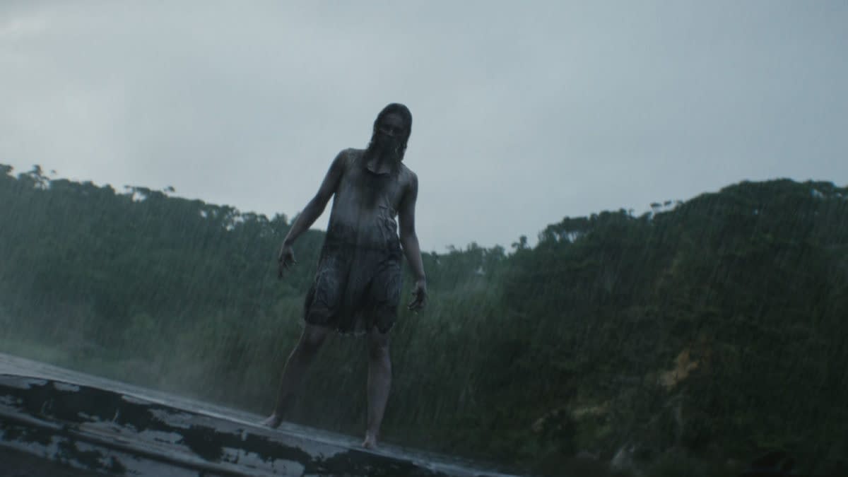 A rain-soaked, eerie figure stands on a rooftop or platform in a dark forest, evoking a creepy Evil Dead Burn horror scene.