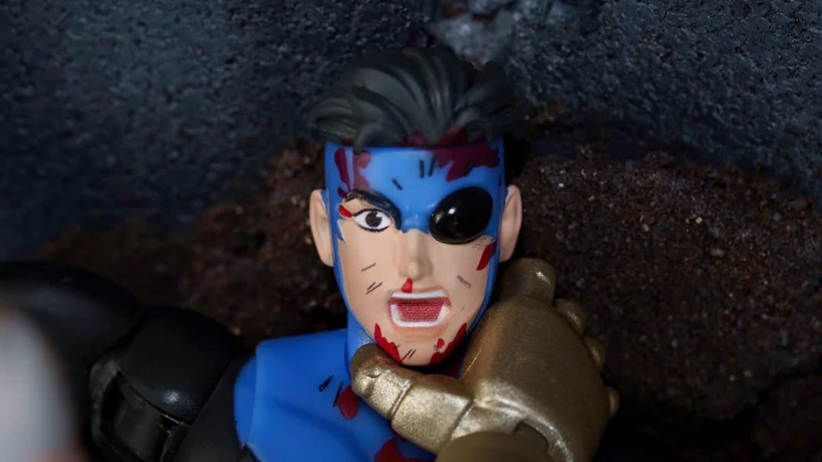 Close-up of a battle-damaged Invincible action figure with a blue-and-black costume, blood marks, and one damaged eye. The figure appears posed in a gritty, dramatic scene.