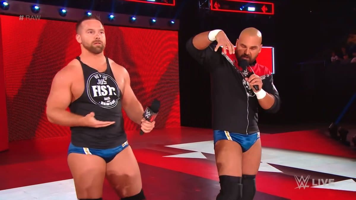FTR stand in a WWE Raw ring, each holding a microphone during a promo segment. The red stage lighting and WWE Live graphics frame the moment.