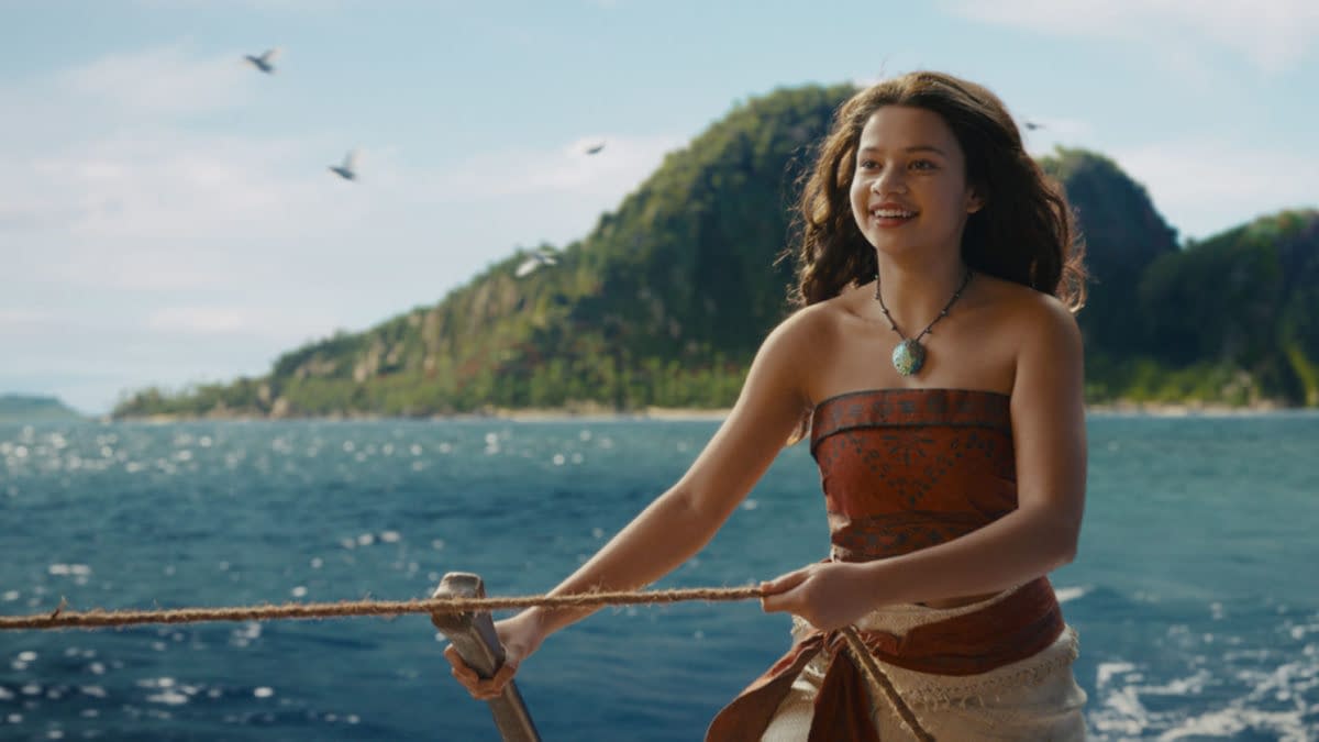 Catherine Laga'aia as Moana smiles while steering a boat across the ocean in Disney's live-action Moana, with tropical islands in the background.