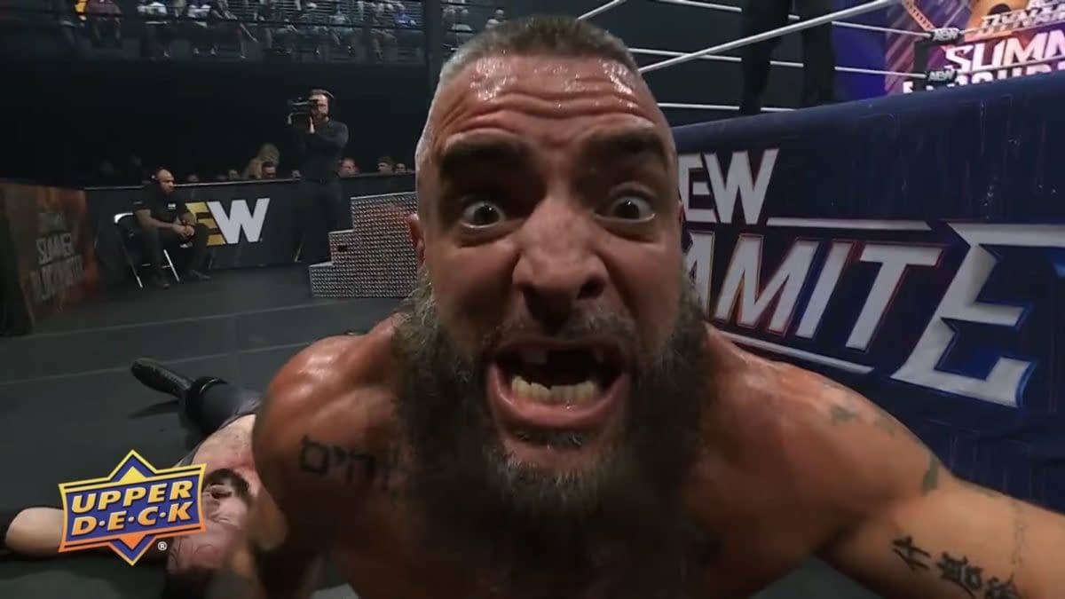 Mark Briscoe yells intensely into the camera at ringside during AEW Dynamite, with a fallen opponent behind him. The AEW Summer Blockbuster backdrop is visible in the background.