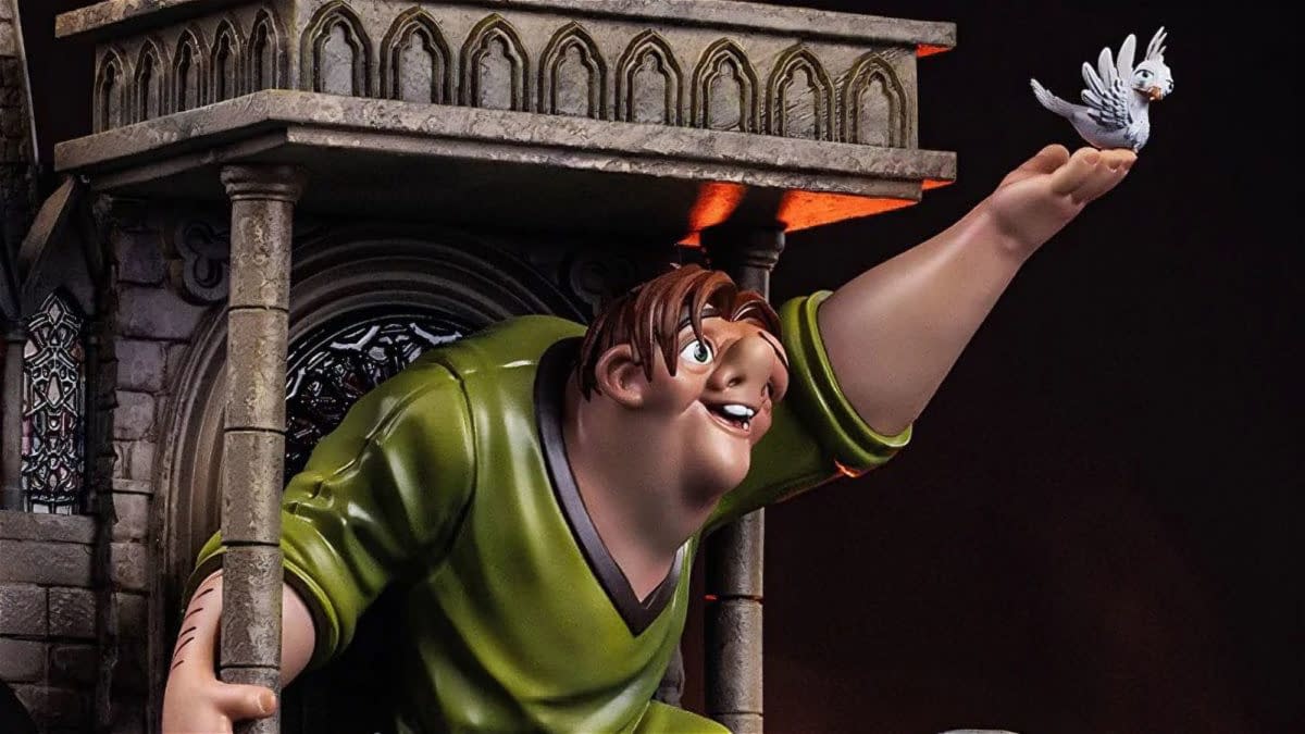 Disney’s Hunchback of Notre Dame statue of Quasimodo reaching out toward a small dove beside a Gothic cathedral balcony. The figure is shown in a dramatic, action pose against a dark background.