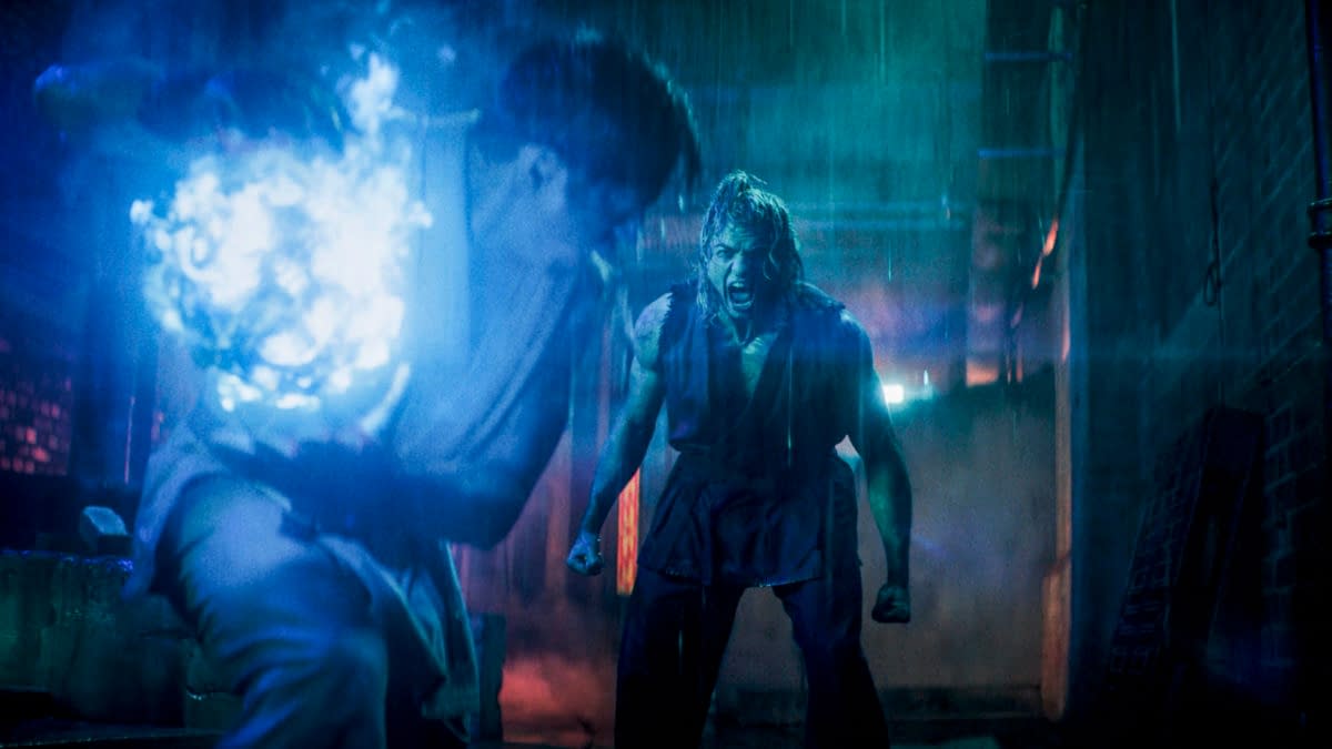 Promotional still from Street Fighter showing two men in a neon-lit alley, one lunging in the foreground while the other screams with clenched fists.