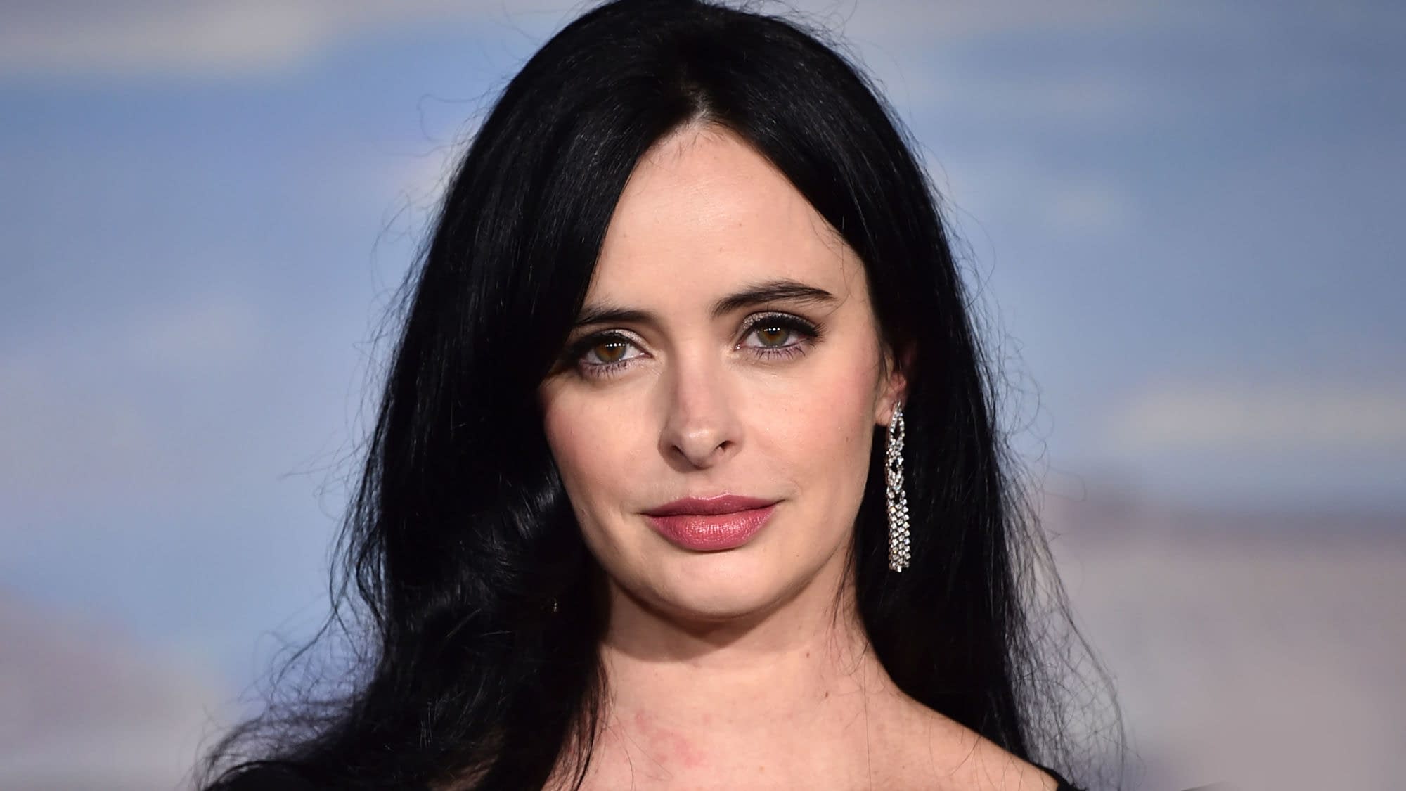 Krysten Ritter poses on the red carpet at the Los Angeles premiere of El Camino: A Breaking Bad Movie, wearing long black hair and dangling earrings.