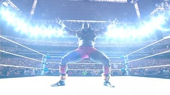 A wrestler in pink shorts and black boots poses dramatically in a brightly lit arena, surrounded by a cheering crowd. The atmosphere is electric, highlighting the intensity of the moment.