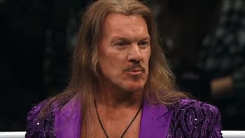 Chris Jericho, wearing a vibrant purple outfit, is featured in a wrestling ring. He has long hair and is giving a serious expression, indicating a dramatic moment.