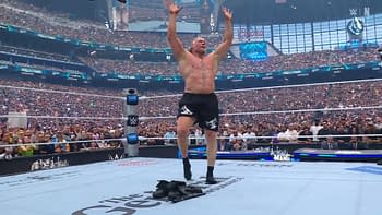 A muscular wrestler, Brock Lesnar, stands in the center of a wrestling ring, raising both hands in the air. A large crowd can be seen cheering in the background, with signs and banners visible among the fans.