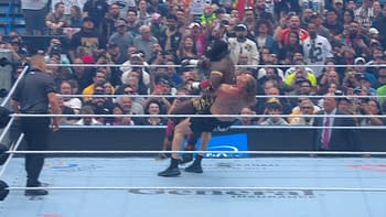 A wrestler lifts another in a dramatic move during a match at WrestleMania, with fans cheering in the background. The scene captures the intensity and excitement of the event.