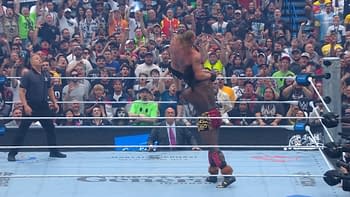 A professional wrestling match featuring a wrestler lifting another above his head, while the crowd around the ring is highly engaged and cheering loudly. The scene captures the excitement of a key moment in the event.