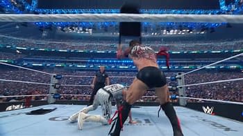 A wrestler with intricate tattoos raises a steel chair to strike another wrestler who is crouched on the ring floor, under bright lights and in front of a large cheering crowd.