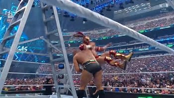 A wrestling scene where one wrestler is executing a powerful move on another, with a ladder prominently displayed in the foreground. The audience is visible in the background, showing a large crowd in an arena setting.