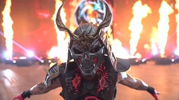 An intense character in a skull mask and elaborate costume stands confidently amid flames and vibrant lighting. The atmosphere suggests a dramatic wrestling event.