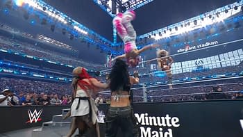 A high-energy wrestling scene at WrestleMania, with a wrestler in pink and white performing a flip above the ring. Spectators and colorful lighting fill the stadium in the background.