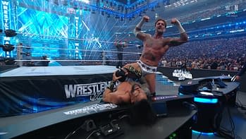 In a dramatic moment from a wrestling match, a muscular athlete celebrates after a decisive victory, flexing his muscles while his opponent lies on the ground. The backdrop shows a vibrant arena filled with bright lights and an enthusiastic crowd.