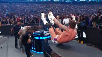 A wrestler executes a high-impact move during a live event, with a vibrant crowd in the background capturing the excitement of the moment. The performer is airborne, showcasing athleticism and energy in the ring.