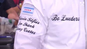 A person wearing a white jacket with names embroidered on the sleeves, including 'Bo Lueders' and other names, along with a Chicago city flag patch.