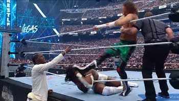 A wrestling match at WrestleMania shows Trick Williams delivering a kick to an opponent on the mat, while a third figure in a white shirt reacts from the sidelines. The arena is filled with a large audience and bright lights in the background.