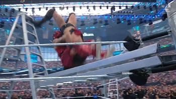 A wrestler in a red outfit is performing a high-flying move off a ladder in a wrestling ring, with an audience visible in the background.