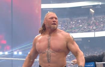 A muscular wrestler stands in a wrestling ring, wearing black shorts, with a focused expression. He has a prominent tattoo of a sword on his chest, and the arena lights create an energetic atmosphere.