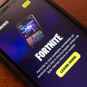 A close-up view of a mobile phone displaying the Fortnite app interface, featuring vibrant graphics and a prominent 'Learn More' button. The screen shows information about the game's availability on mobile devices.