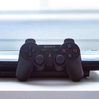 A Playstation PS3 with a control remote on a white table. Editorial credit: oasisamuel / Shutterstock.com