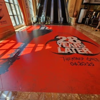 A vibrant red promotional floor graphic for the film '28 Years Later,' featuring a large silhouette of a chainsaw and bold text announcing its release date, June 20, 2025.