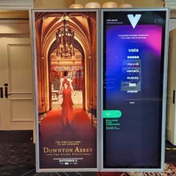 A promotional display for 'Downton Abbey: The Grand Finale' featuring a woman in a flowing red dress walking through an ornate archway. The display is set in a movie theater lobby, showcasing the movie's release date.