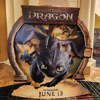 A promotional standee for 'How to Train Your Dragon' featuring the dragon character Toothless in flight, surrounded by other dragons and a scenic background. The text announces the film's release date as June 13.